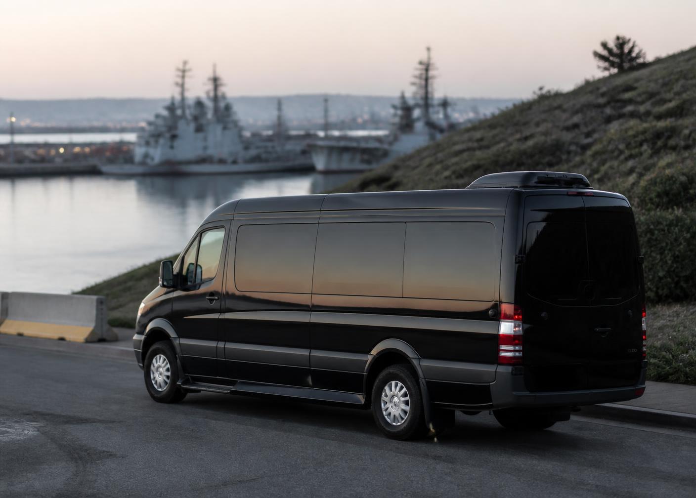 Dark passenger van parked near the San Diego naval waterfront at dawn